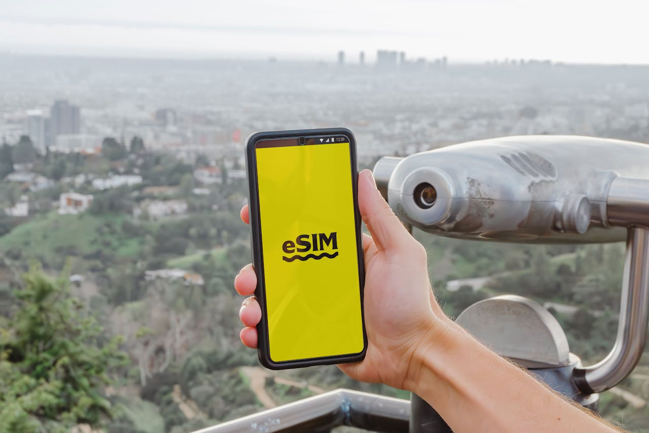 A hand holding an eSIM-enabled smartphone at a scenic viewpoint overlooking Los Angeles, California.